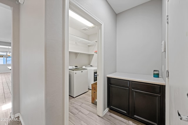 clothes washing area with laundry area, washing machine and dryer, baseboards, and wood tiled floor