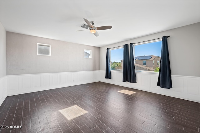 empty room with ceiling fan, wainscoting, dark wood-style flooring, and visible vents