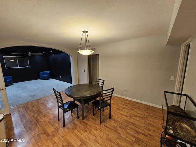 dining space featuring light wood finished floors, baseboards, arched walkways, and a textured ceiling