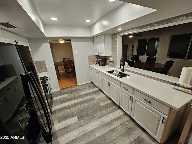 kitchen with a peninsula, a sink, visible vents, light wood-style floors, and decorative backsplash