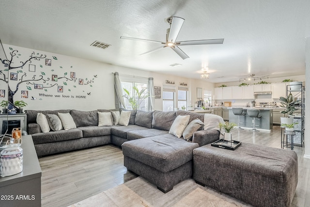living area with a ceiling fan, visible vents, and light wood-type flooring