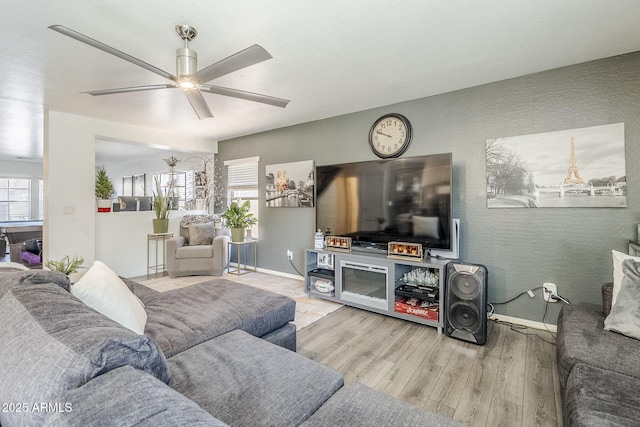 living area featuring plenty of natural light, a ceiling fan, baseboards, and wood finished floors