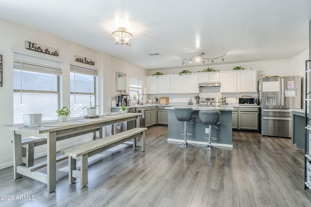kitchen with under cabinet range hood, wood finished floors, light countertops, a chandelier, and stainless steel appliances