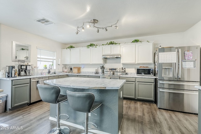 kitchen featuring a breakfast bar area, visible vents, wood finished floors, light countertops, and stainless steel appliances