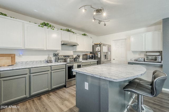 kitchen featuring appliances with stainless steel finishes, a breakfast bar area, gray cabinets, light wood-style flooring, and under cabinet range hood