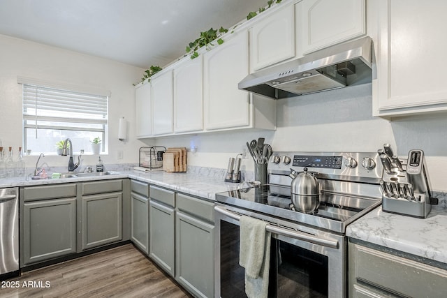 kitchen with appliances with stainless steel finishes, a sink, gray cabinets, white cabinetry, and under cabinet range hood