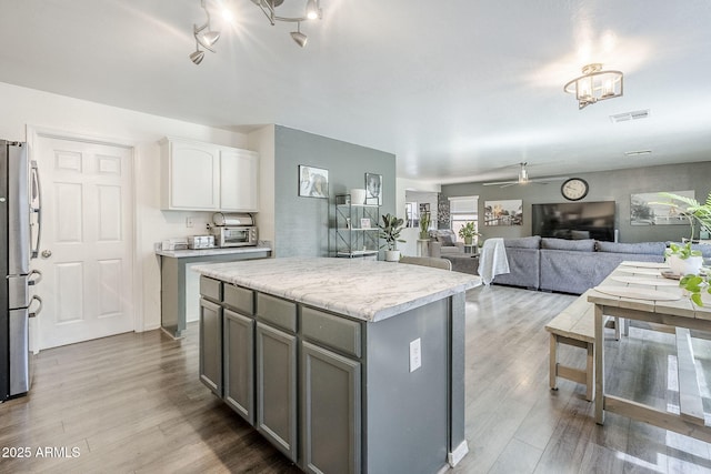 kitchen featuring visible vents, freestanding refrigerator, a kitchen island, ceiling fan, and gray cabinetry