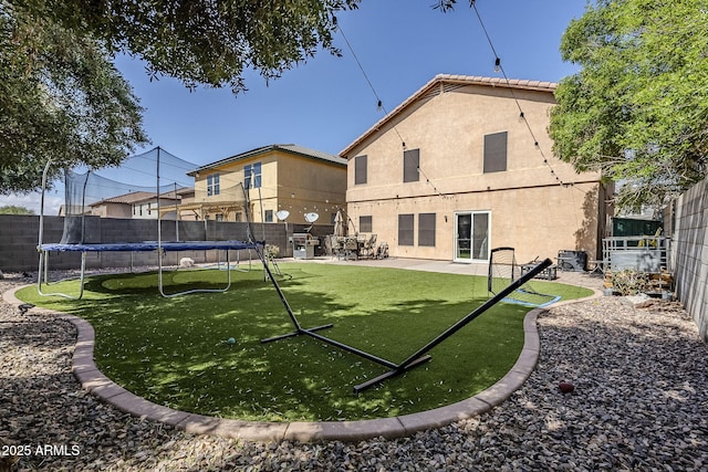 back of property with a lawn, a fenced backyard, a trampoline, and stucco siding