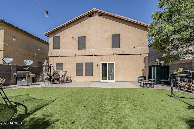 rear view of property featuring stucco siding, a lawn, fence, and an outdoor fire pit