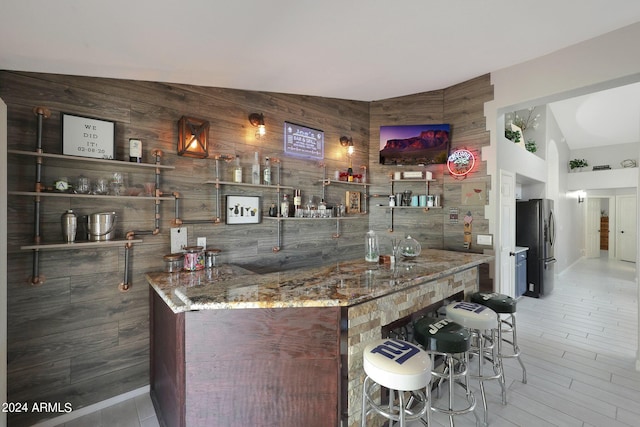 bar featuring stone countertops and stainless steel fridge