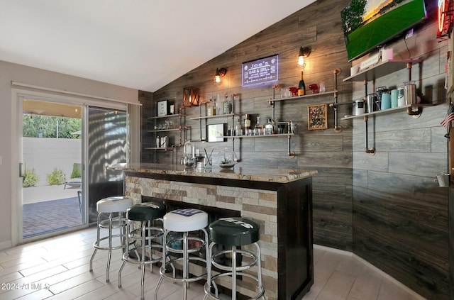 bar featuring lofted ceiling and wooden walls