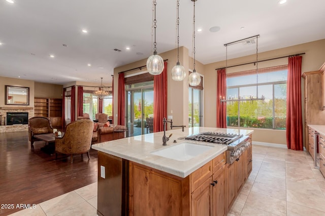 kitchen with sink, an inviting chandelier, decorative light fixtures, a center island with sink, and stainless steel gas stovetop