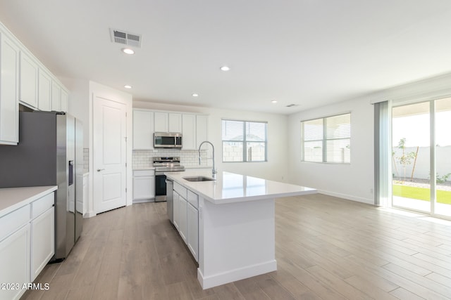 kitchen featuring light wood-type flooring, white cabinetry, appliances with stainless steel finishes, sink, and an island with sink