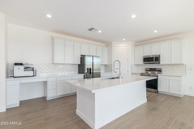 kitchen with stainless steel appliances, white cabinetry, sink, and an island with sink