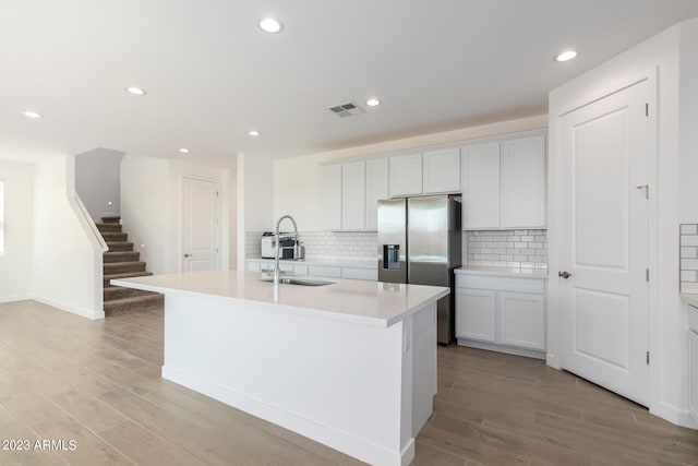 kitchen featuring sink, an island with sink, backsplash, and white cabinetry