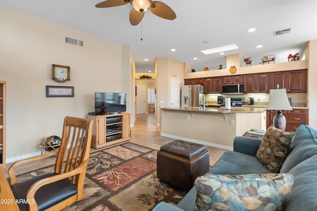 living room with ceiling fan, a towering ceiling, and a skylight