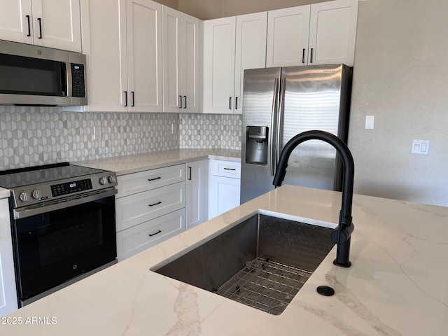 kitchen featuring light stone countertops, a sink, decorative backsplash, white cabinets, and appliances with stainless steel finishes