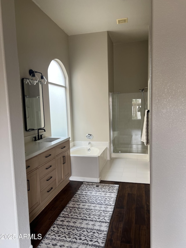 full bath featuring a stall shower, wood finished floors, vanity, and a bath