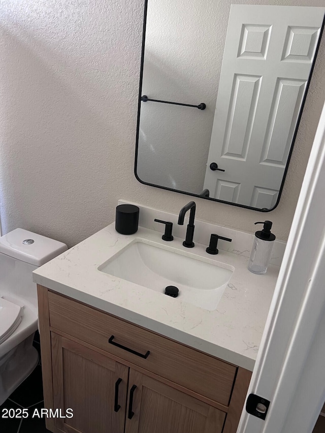 bathroom featuring vanity, toilet, and a textured wall