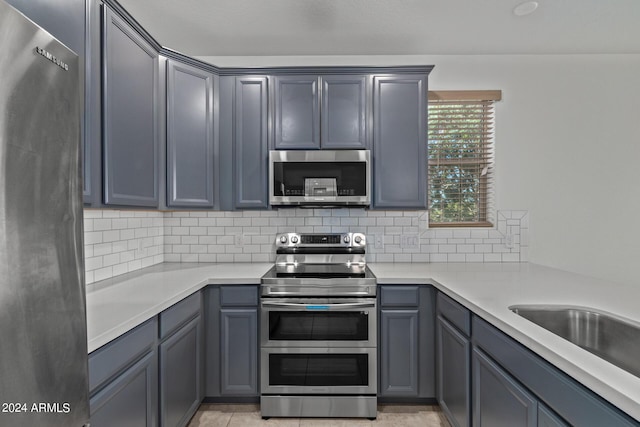 kitchen featuring decorative backsplash, light tile patterned floors, stainless steel appliances, and gray cabinetry