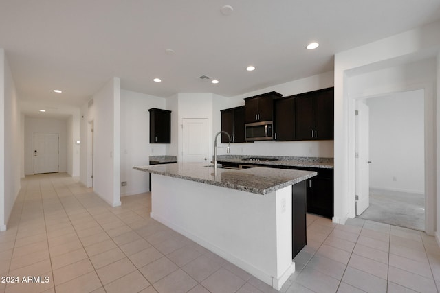 kitchen featuring light stone countertops, stainless steel appliances, a kitchen island with sink, sink, and light tile patterned floors