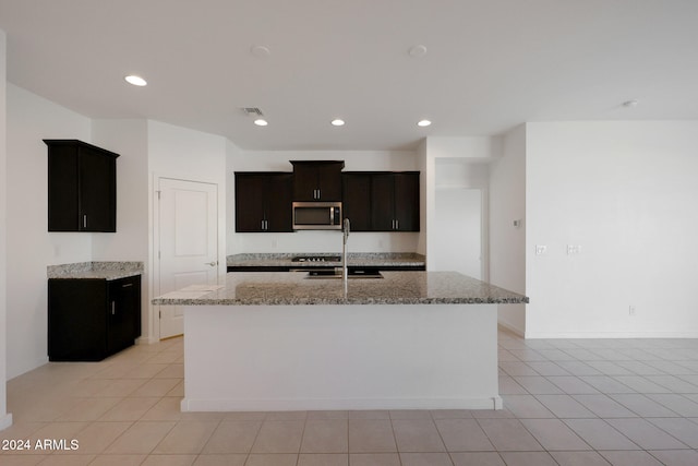 kitchen featuring a center island with sink, light stone countertops, sink, and light tile patterned floors