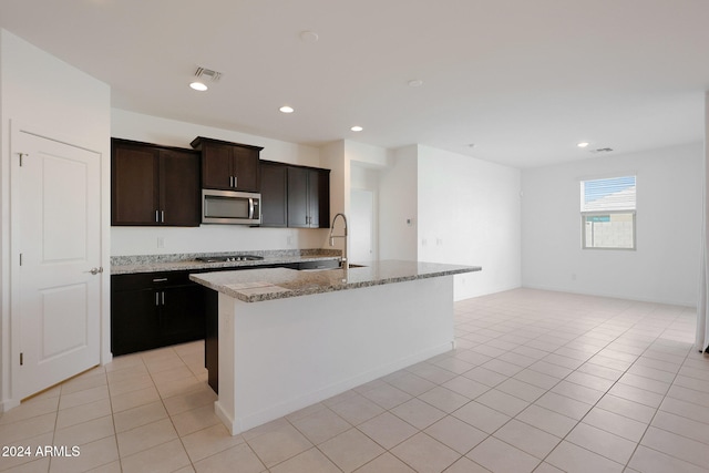 kitchen featuring appliances with stainless steel finishes, light stone counters, sink, light tile patterned floors, and an island with sink