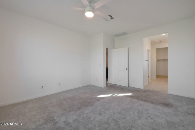 unfurnished bedroom featuring light carpet, a walk in closet, a closet, and ceiling fan