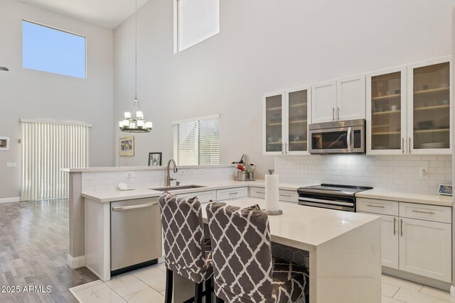 46141 W Rainbow Dr, Maricopa, AZ 85139 - kitchen with stainless steel appliances, a towering ceiling, a peninsula, tasteful backsplash, and light countertops