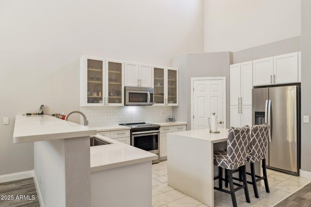 46141 W Rainbow Dr, Maricopa, AZ 85139 - kitchen with appliances with stainless steel finishes, a breakfast bar, a peninsula, white cabinetry, and a towering ceiling