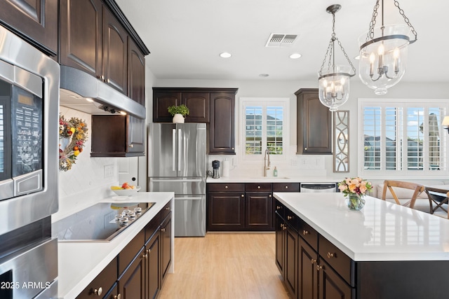 kitchen with light wood-style floors, a sink, light countertops, an inviting chandelier, and stainless steel appliances