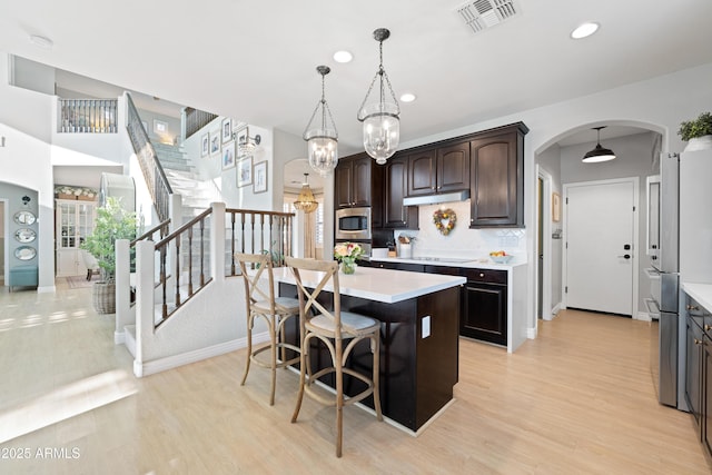 kitchen featuring visible vents, light countertops, under cabinet range hood, arched walkways, and appliances with stainless steel finishes