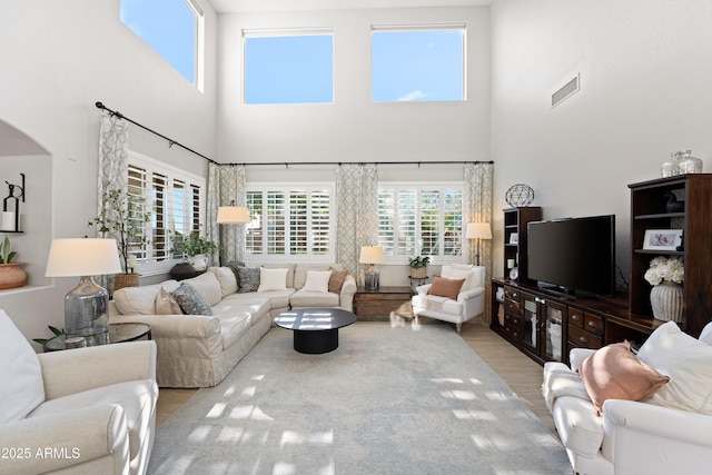 living room featuring arched walkways, visible vents, wood finished floors, and a towering ceiling