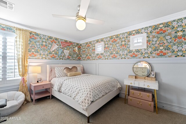 carpeted bedroom featuring visible vents, ornamental molding, wainscoting, wallpapered walls, and a ceiling fan
