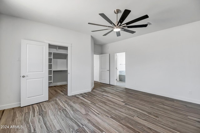 unfurnished bedroom with a walk in closet, ceiling fan, a closet, and wood-type flooring