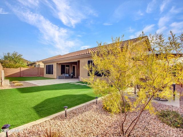 rear view of property featuring a lawn, a patio, a tile roof, fence, and stucco siding