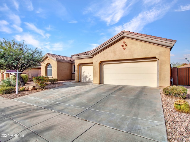 mediterranean / spanish house with a garage, fence, a tile roof, concrete driveway, and stucco siding