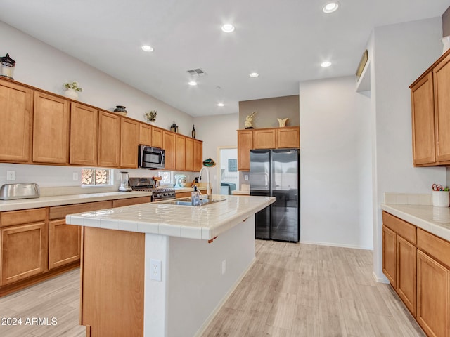 kitchen featuring a center island with sink, sink, appliances with stainless steel finishes, tile counters, and light hardwood / wood-style floors