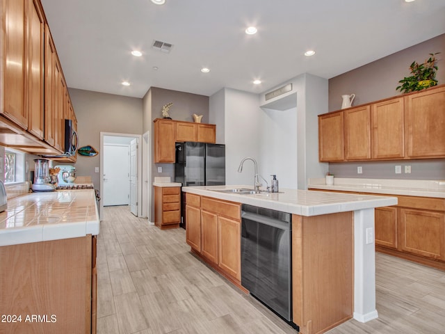 kitchen with tile countertops, stainless steel appliances, a kitchen island with sink, and sink