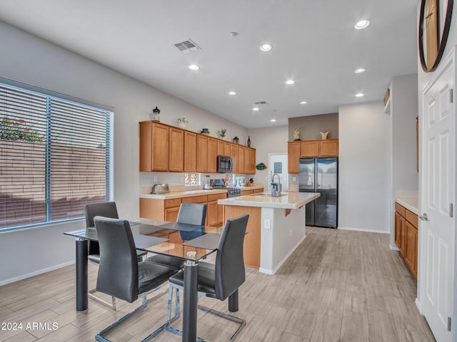 kitchen featuring sink, a kitchen breakfast bar, light hardwood / wood-style floors, a center island with sink, and black appliances