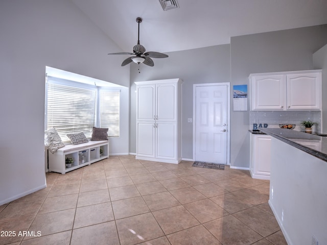 interior space with vaulted ceiling, backsplash, white cabinets, light tile patterned floors, and ceiling fan