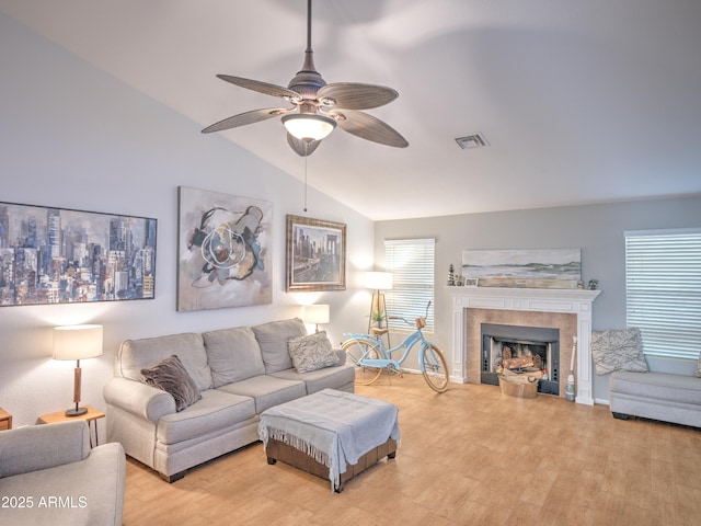 living room featuring ceiling fan, lofted ceiling, a tile fireplace, and light hardwood / wood-style flooring