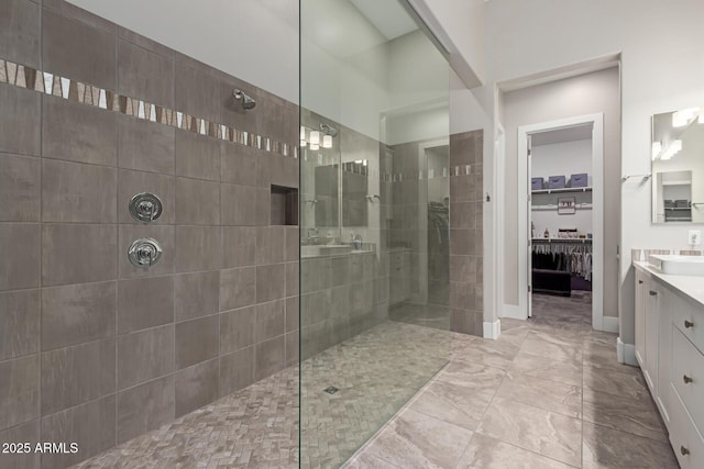 full bathroom with a spacious closet, a walk in shower, vanity, and baseboards