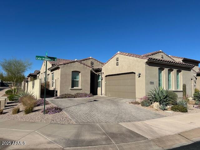 mediterranean / spanish home featuring a tiled roof, decorative driveway, an attached garage, and stucco siding