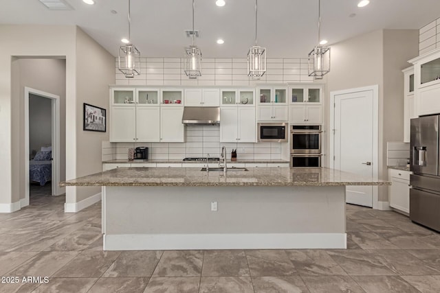 kitchen featuring a sink, under cabinet range hood, decorative backsplash, appliances with stainless steel finishes, and a kitchen island with sink