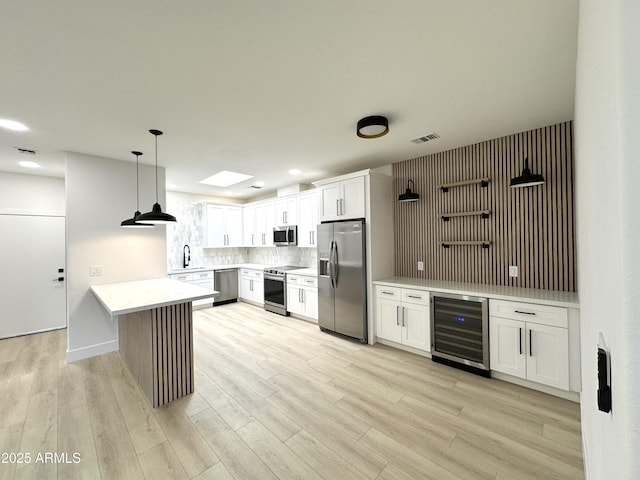 kitchen with a peninsula, beverage cooler, light wood finished floors, appliances with stainless steel finishes, and tasteful backsplash