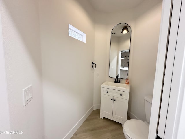 half bathroom featuring toilet, baseboards, vanity, and wood finished floors
