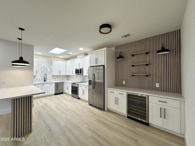 kitchen featuring stainless steel appliances, a skylight, visible vents, backsplash, and wine cooler