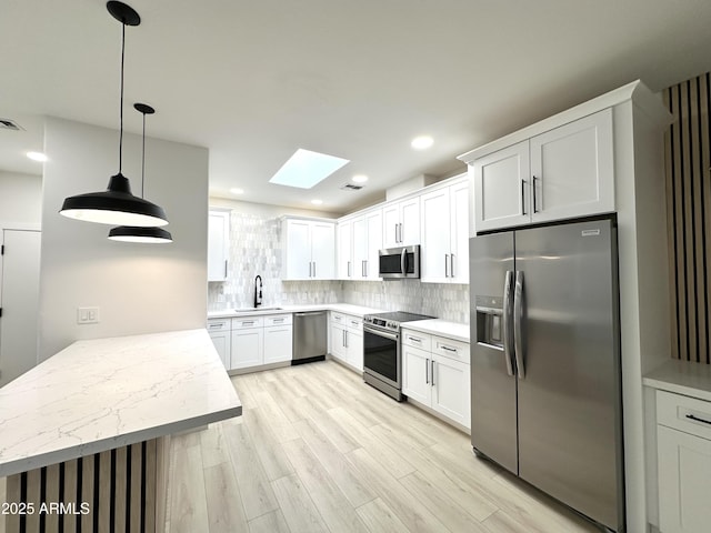 kitchen with light wood-style flooring, a sink, stainless steel appliances, tasteful backsplash, and a skylight