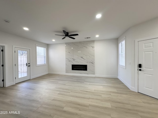 unfurnished living room featuring light wood finished floors, a ceiling fan, a premium fireplace, baseboards, and recessed lighting